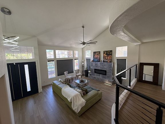 Living area featuring wood finished floors, fireplace, high vaulted ceiling, and a ceiling fan