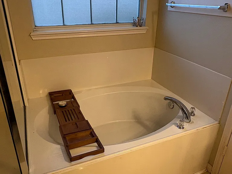Bathroom features a soaking tub/shower combo with tiled surround, frosted window for privacy, and convenient towel bar.