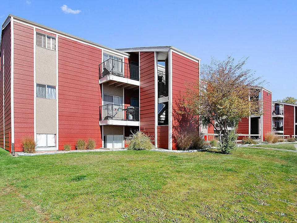 Charming red apartment complex with private balconies, nestled in a lush green landscape, perfect for modern living.