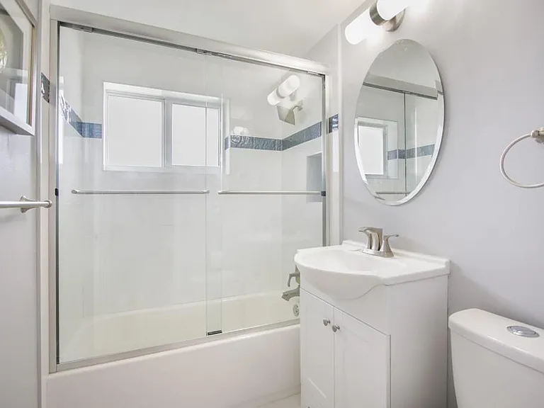 Full bathroom with tub/shower combo, sliding glass doors, vanity storage, and an updated mirror with wall lighting.