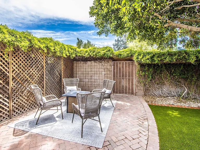 Patio relaxation at Casa Del Sol, Tempe rental home. Features an outdoor chat set with four woven armchairs, an outdoor rug, a fire pit table, brick pavers, and a putting green. Ideal backyard retreat for a top Tempe, AZ vacation stay.
