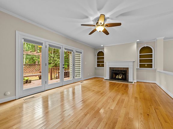Light-filled living room with hardwood floors, fireplace, crown molding, and French doors to the deck.