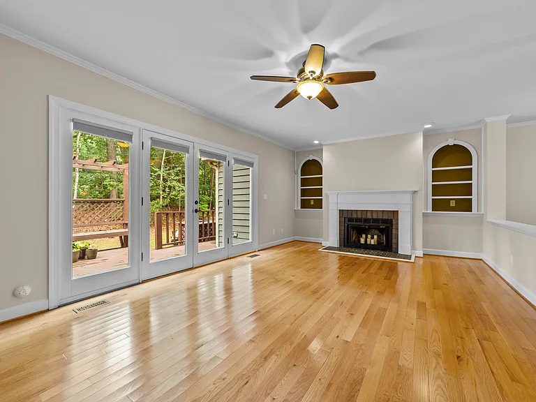 Light-filled living room with hardwood floors, fireplace, crown molding, and French doors to the deck.
