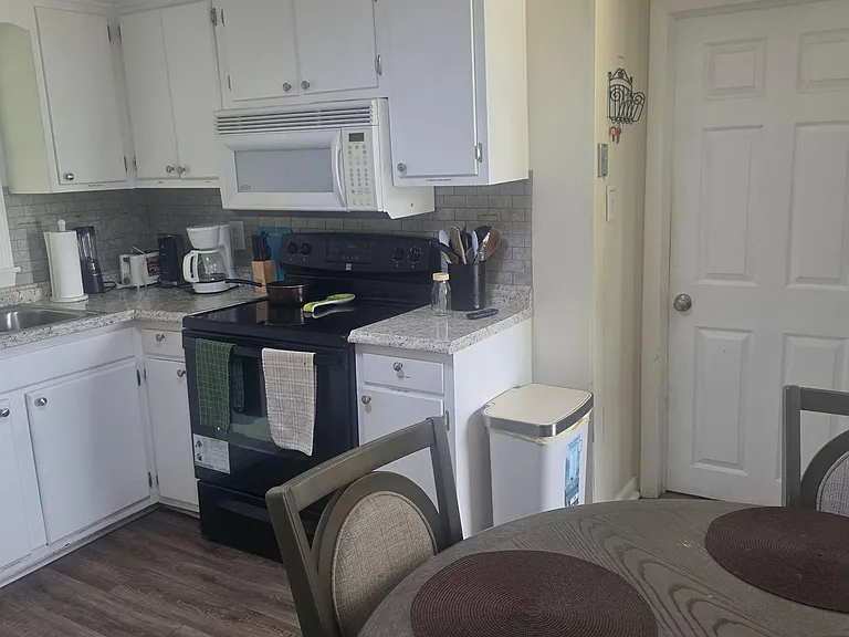 Efficient kitchen with ample white cabinetry, laminate counters, electric range with over-the-range microwave, and nearby din