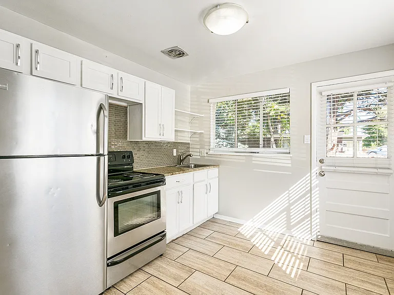 Bright kitchen with stainless steel appliances, white cabinetry, and large window offering natural light.