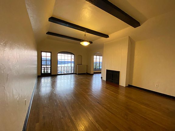 Spacious living room with direct western Lake Union and sunset views, wood burning fireplace, hardwood floor, balcony access, and dining room entry.