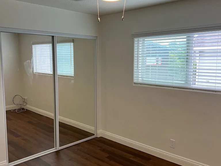 Bedroom with brand new paint, Brand new white blinds, brand new ceiling light fan, brand new mirrored closet doors, lots of storage inside closet and wood laminate flooring