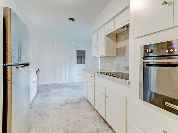 Kitchen with new flooring. Wall oven and smooth surface electric cooktop installed in 2021, along with wonderful metallic backsplash. Stainless Steel refrigerator too. Door leads to garage.