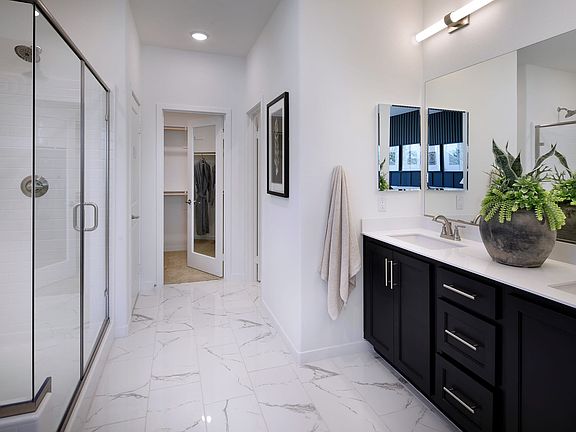 A modern and spacious bathroom with a marble-tiled floor, a dark wooden vanity, and a large mirror o