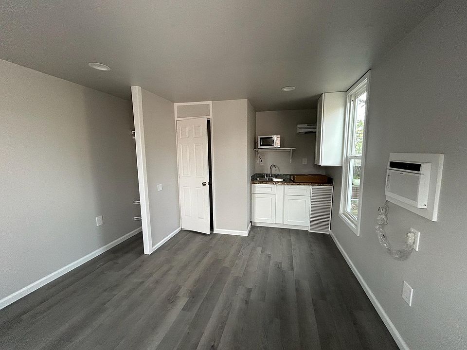 left side is a small closet (includes hangers), bathroom next to it, and kitchen area in back right. Window looks into backyard, a small tree is at sight first.