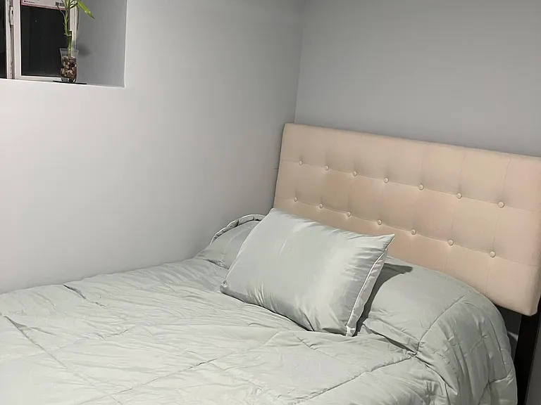 Furnished bedroom featuring a full bed with upholstered headboard, neutral walls, and a window for natural light.