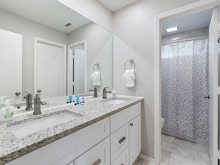 Bathroom with double vanity, marble look tile flooring, and a shower with curtain