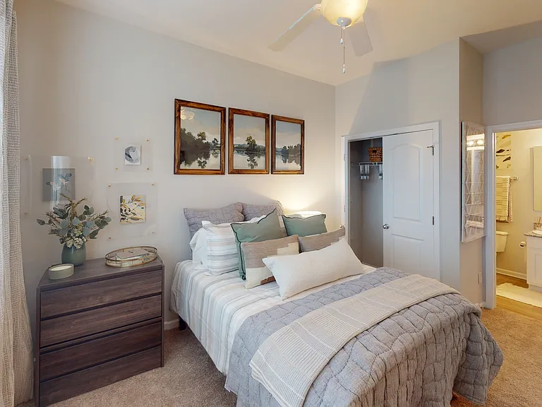 A cozy bedroom at Ralston Apartments in Downtown Indianapolis, featuring soft decor, plush bedding, and an ensuite bathroom with modern finishes.