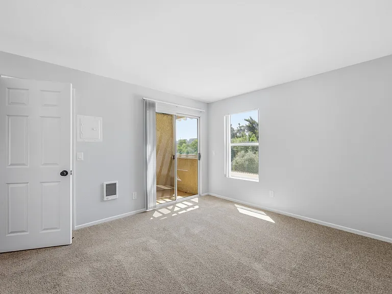 A room with a white door, carpeted floor, and a window with a view of the outdoors.