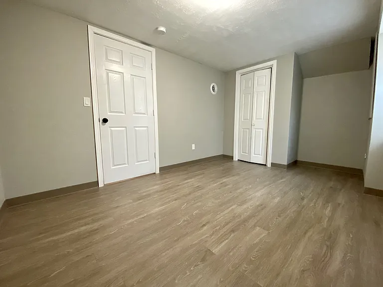 Spacious room with elegant hardwood flooring, featuring two pristine white doors for added storage options. Spacious room with elegant hardwood flooring, featuring two pristine white doors for added storage options.