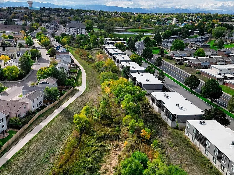 Scenic aerial view of a vibrant suburban neighborhood with lush greenery, winding pathways, and distant mountains, ideal for tranquil living.