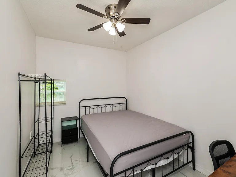 Private bedroom with a ceiling fan, window blinds, and space for a bed plus storage shelving and a small desk area.