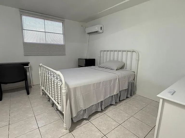 Private bedroom with tiled floors, a single bed, window with blinds, and a dedicated desk area plus mini fridge and AC.