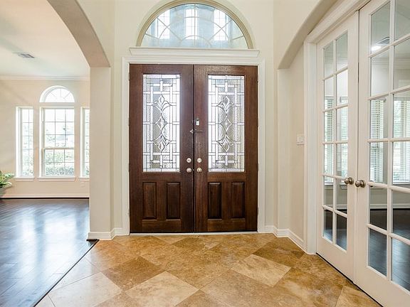 The entry has soaring ceilings with travertine flooring. A view looking back at the double doors with overhead palladium window. The formal dining room is on the left and the study sits behind the French doors.
