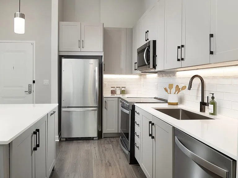 Upgrade Collection II kitchen with stainless steel appliances, grey cabinetry, white quartz countertops, tile backsplash, under-cabinet lighting, and hard surface flooring