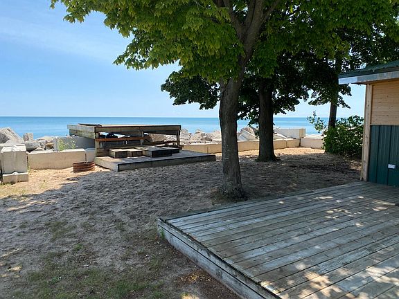 Front yard facing Lake Huron. The deck that is off the master BR and the living room in the foreground and the elevated deck assembled over the retaining wall. Lots of shade from mature trees and a sandy lake bottom as far as you can go.