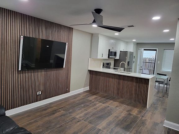 Open-concept living area featuring wood-finish accent wall, contemporary ceiling fan, and large format tile flooring