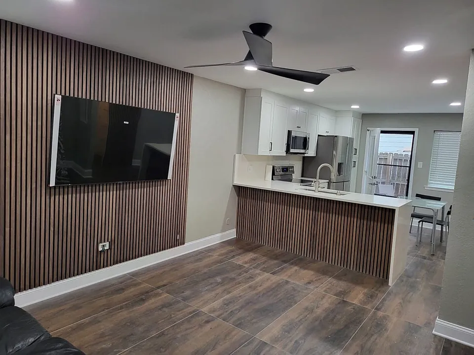 Open-concept living area featuring wood-finish accent wall, contemporary ceiling fan, and large format tile flooring