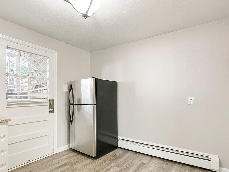 Bright kitchen space featuring modern stainless steel fridge, large window with natural light, and sleek laminate flooring.