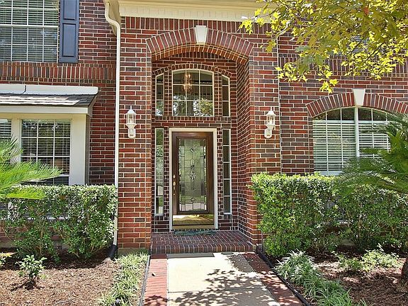 A brick-lined walkway leads to the stunning entry, which features a leaded glass door, transom windows, and sidelights. Arches with intricate brickwork and dark shutters add to the architectural detail of the facade.