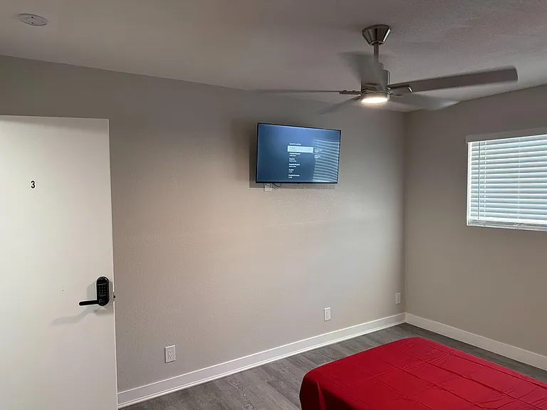 Private bedroom with durable flooring, a ceiling fan, and a wall-mounted TV, plus a window with blinds for light and privacy.