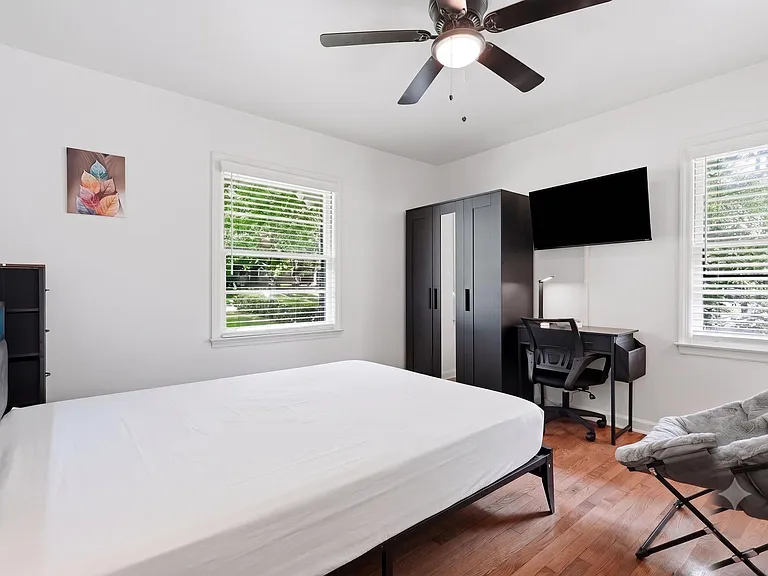 Furnished bedroom with a bed, wardrobe, and dedicated desk area, plus two windows with blinds and a ceiling fan.