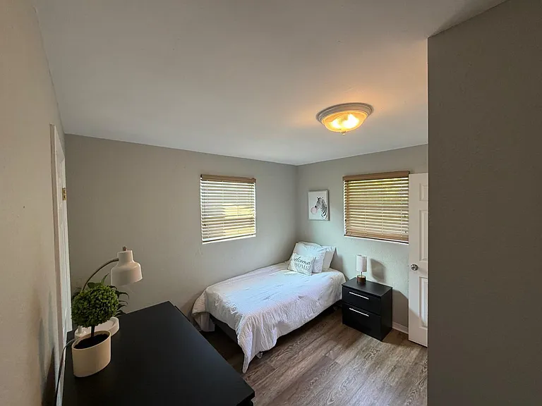 Furnished bedroom with a twin bed, nightstand, and dresser, plus two windows with blinds and durable wood-look flooring.