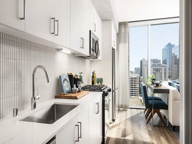 Modern kitchen with sleek white cabinets, stainless steel appliances, and a stunning city view, perfect for urban living.