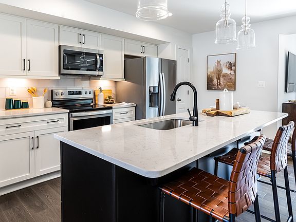 Open kitchen with large island with sink, white cabinets counters, stainless steel appliances, mediu