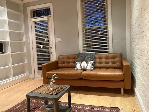 Living room area with exposed brick wall and built-in book shelves across an entire wall. Wood floors.