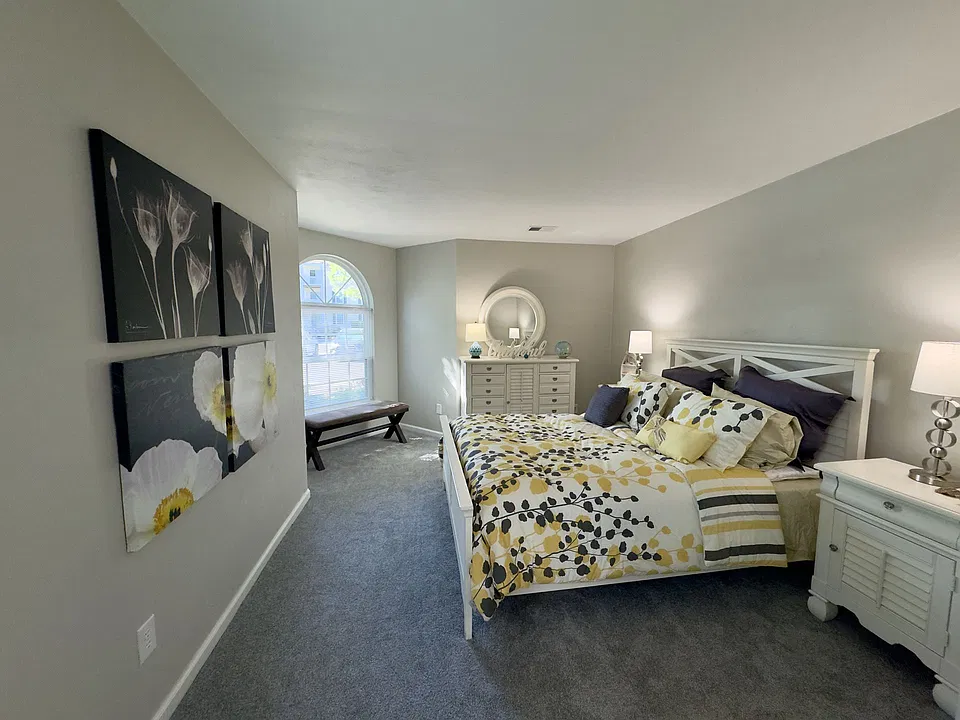 Bright staged bedroom with a full-size bed, patterned bedding, matching nightstands, and a dresser with mirror at North Beach Apartments in Virginia Beach