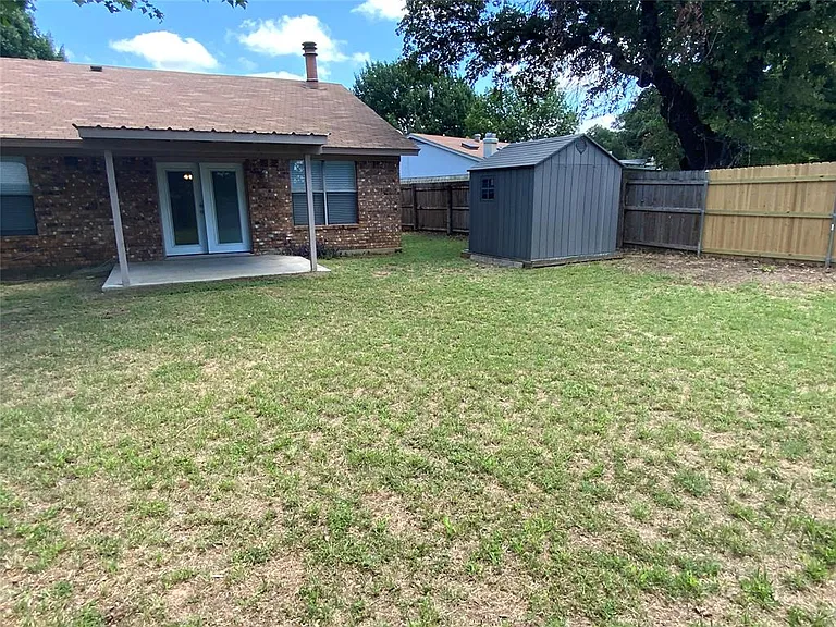 Expansive backyard featuring a covered patio with concrete flooring, dual pane French doors, a gray storage shed, and a privacy fence