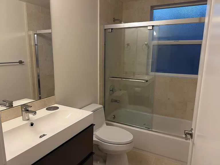 Hallway bathroom is tastefully appointed with granite floor tiles, modern plumbing fixtures and glass shower door.