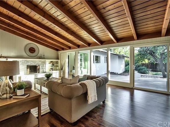 Welcoming entry opens to a stunning living and dining area with soaring open beamed ceilings, a statement fireplace, built-in shelving, and a wall of sliding glass doors that bring the outdoors in.