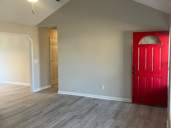 Defined by a striking, vibrant red accent door, the space blends comfort with bold charm, featuring high ceilings and plenty of room for versatile furniture arrangements.