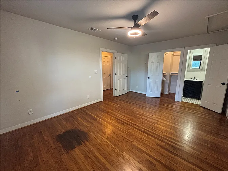Spacious room with wood-finish flooring, light neutral wall tones, and a ceiling fan with integrated lighting
