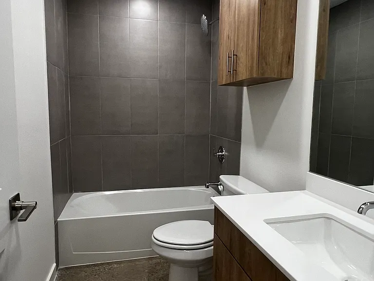 This Hall bath has a large tub, with modern gray tile and stained cabinets. The vanity is extra spacious with plenty of storage and countertop space.