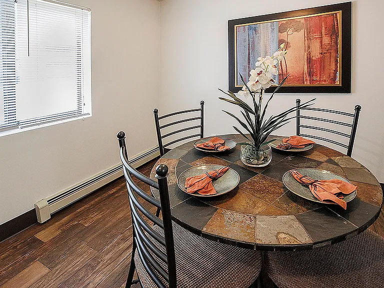 Inviting dining room with a stylish stone tile table, accented by vibrant orange napkins and elegant decor in an intimate setting.