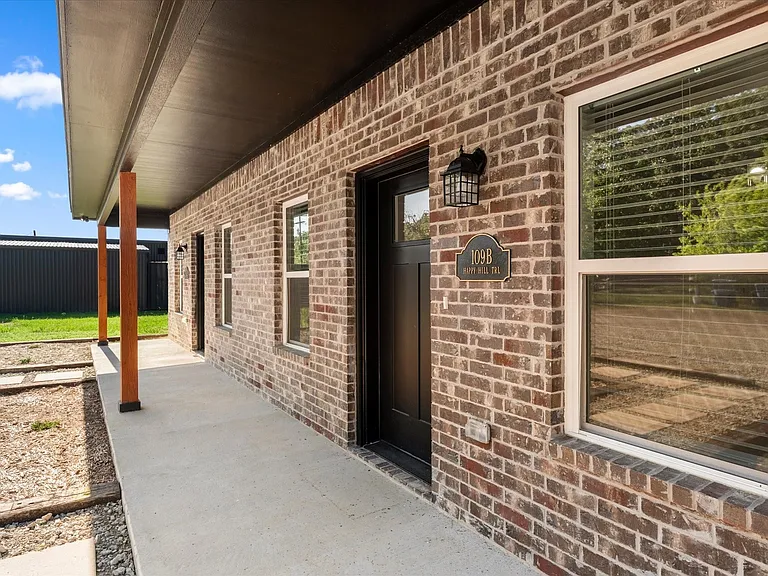 Brick exterior featuring a covered porch with natural wood posts, a solid black entry door, and white-framed windows