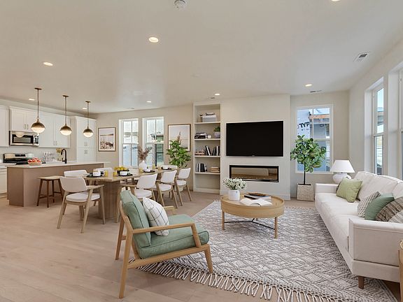 Modern open-concept living and dining area with light wood floors, white walls, a beige sofa, green