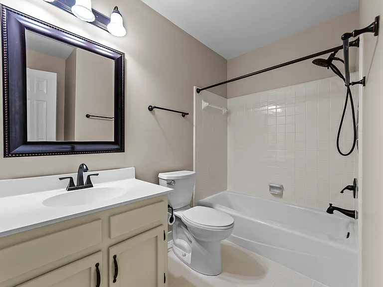 Full bath with tub/shower combo, white vanity, dark hardware, and neutral finishes.