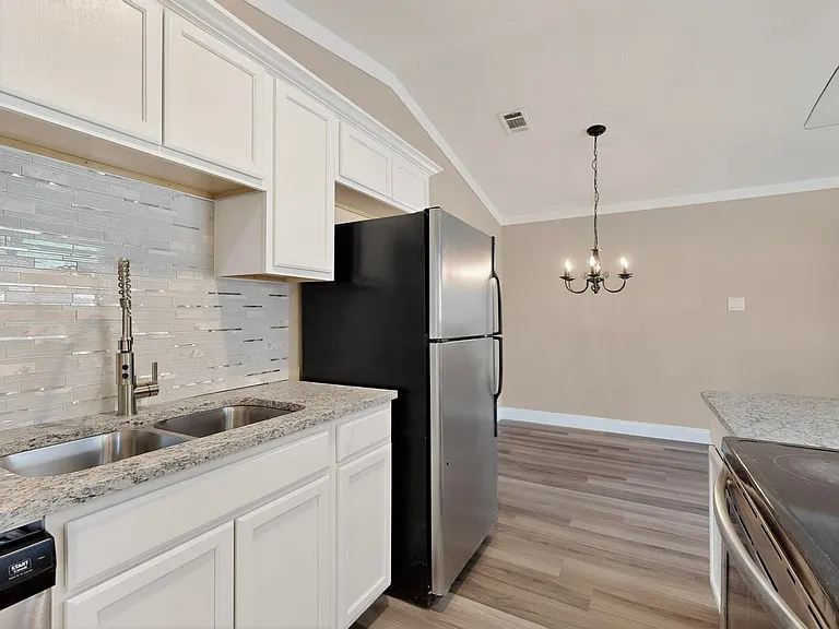 Kitchen featuring backsplash, white cabinetry, light stone countertops, crown molding, and light wood-type flooring