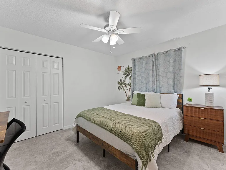 Spacious bedroom with tile flooring, ceiling fan, double-door closet, and a dresser for extra storage.