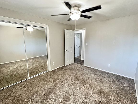 Bright, carpeted bedroom with mirrored closet doors and overhead ceiling fan, offering modern comfort and style.