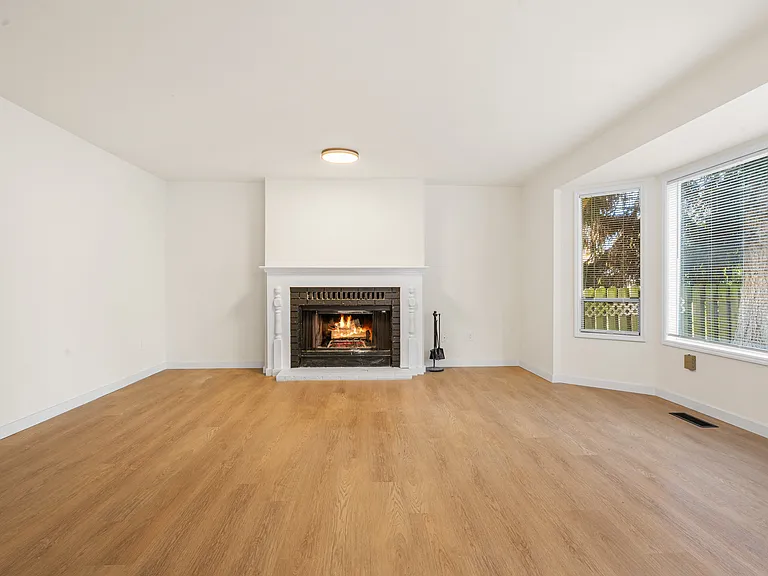 Generous family room filled with natural light, featuring multiple windows and a cozy wood burning fireplace for relaxing evenings.